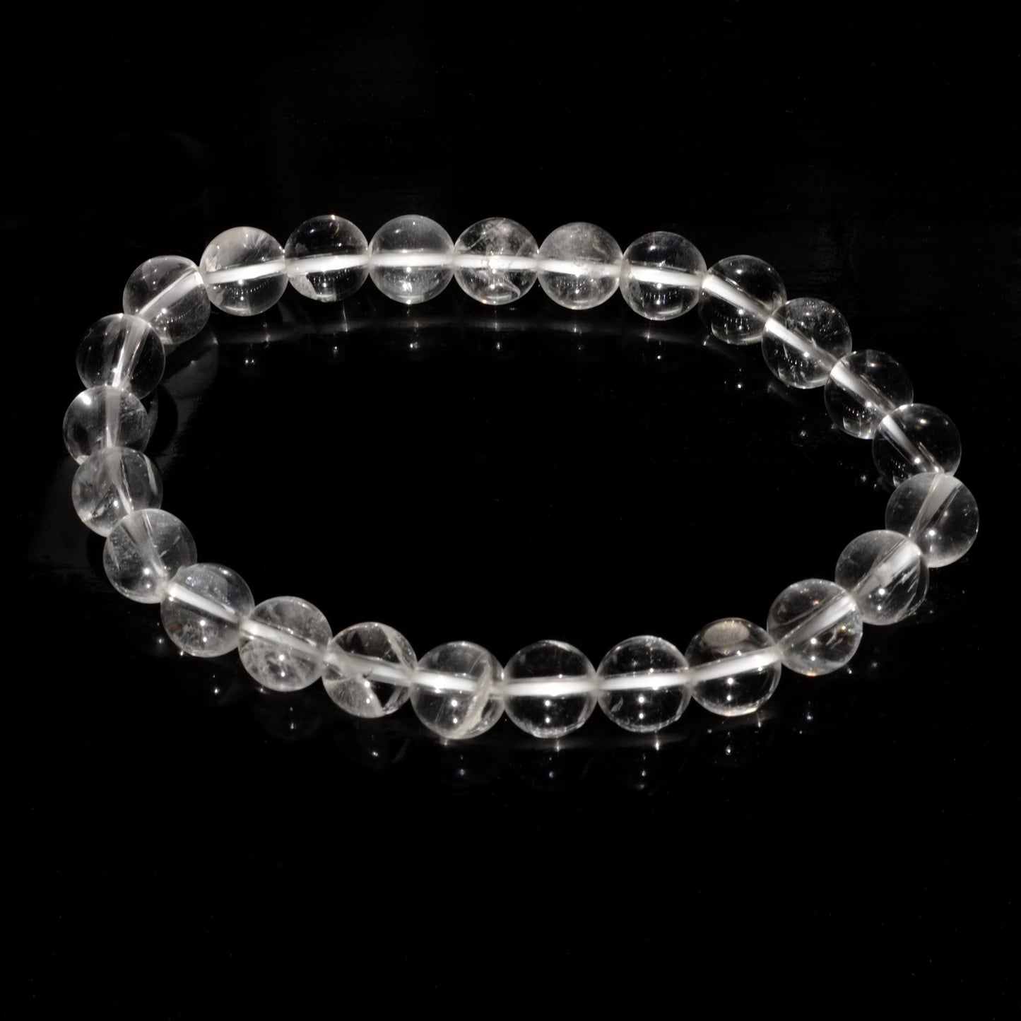 Bracelet boule en cristal de roche du Brésil sur fond noir éclairé par la lumière du soleil.