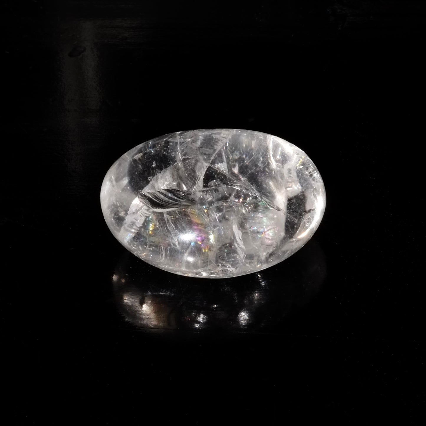 Photo d'une pierre roulée en cristal de roche de qualité AA provenant du Brésil sur fond noir éclairé par la lumière du soleil. Le soleil donne à la pierre de cristal de roche des éclats aux couleurs de l'arc-en-ciel.