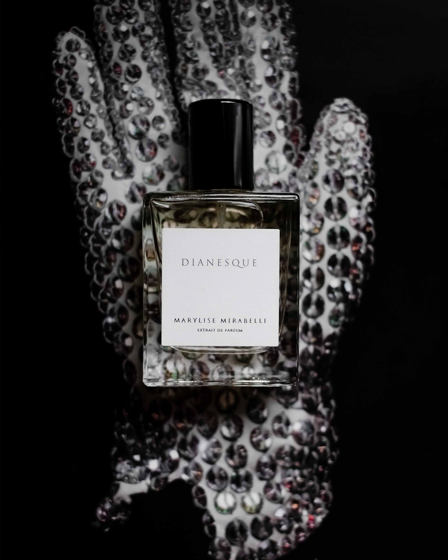 Petit flacon de parfum rectangulaire avec une étiquette blanche, l'inscription Dianesque, et son bouchon noir brillant. Le flacon de 30ml est posé sur le gant à paillettes de Michael Jackson pour représenter l'univers musical et l'inspiration de la collection.