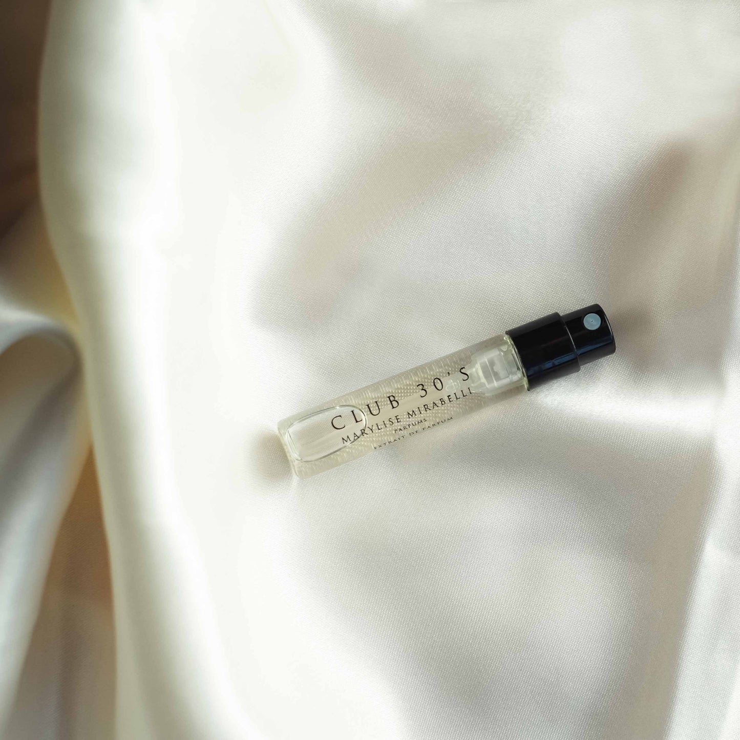Un flacon de parfum en format 2ml du parfum Club 30's est posé sur un tissu en satin blanc.