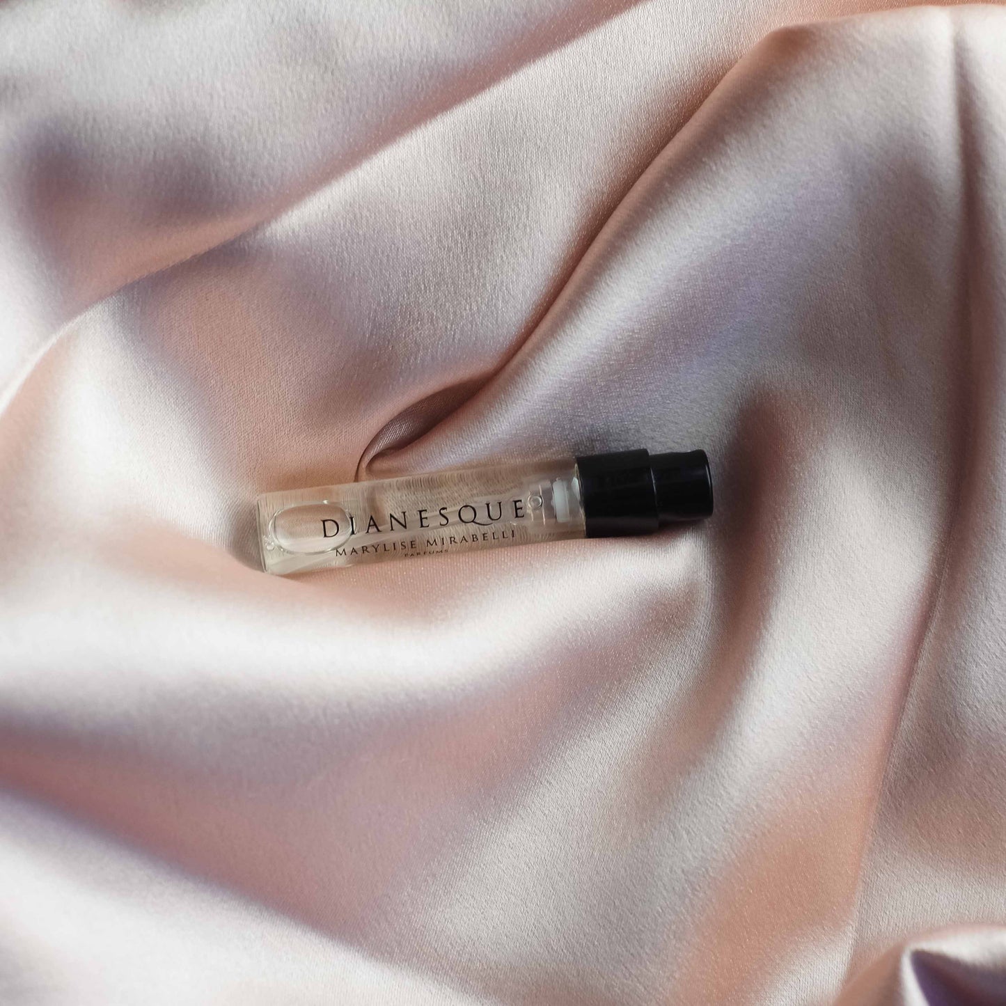 Un flacon de parfum en format 2ml du parfum Dianesque est posé sur un tissu en satin rosé poudré.