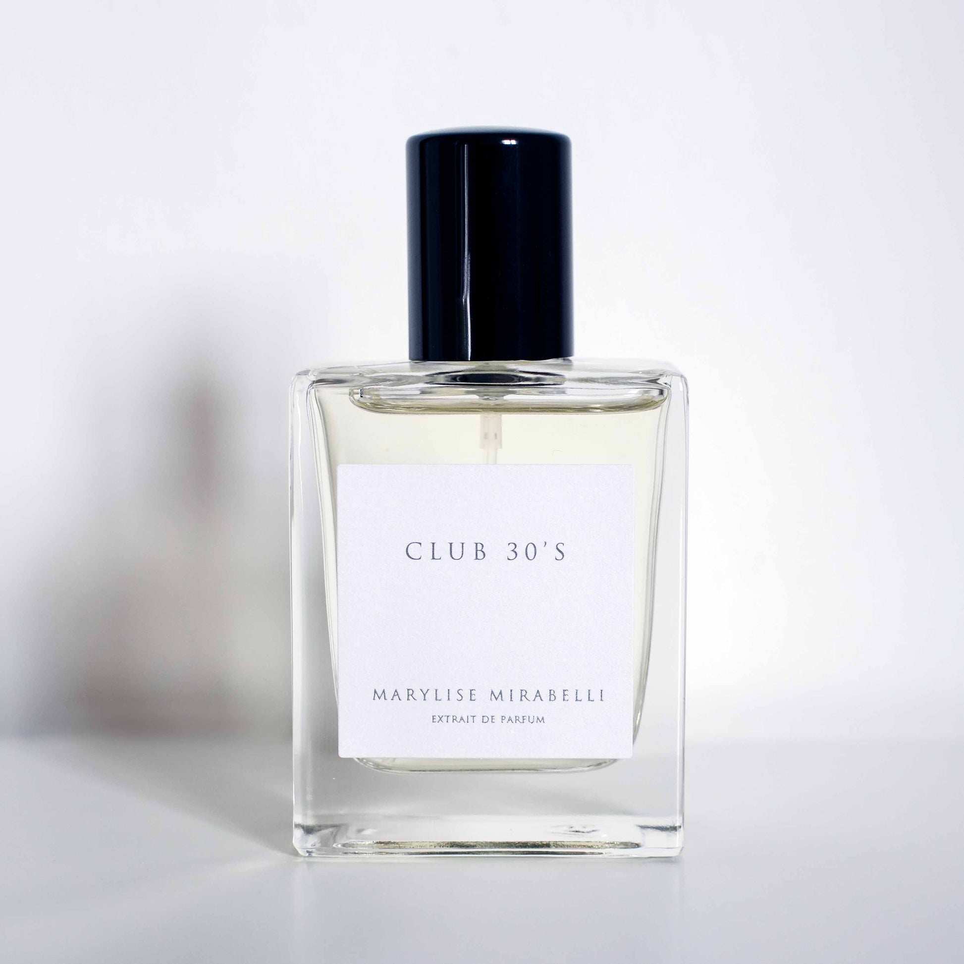 Flacon sobre et rectangulaire avec étiquette blanche et bouchon noir brillant, posé sur un fond blanc. Sur l'étiquette il est inscrit Club 30's en haut et Marylise Mirabelli Extrait de parfum en bas.