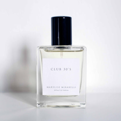 Flacon sobre et rectangulaire avec étiquette blanche et bouchon noir brillant, posé sur un fond blanc. Sur l'étiquette il est inscrit Club 30's en haut et Marylise Mirabelli Extrait de parfum en bas.