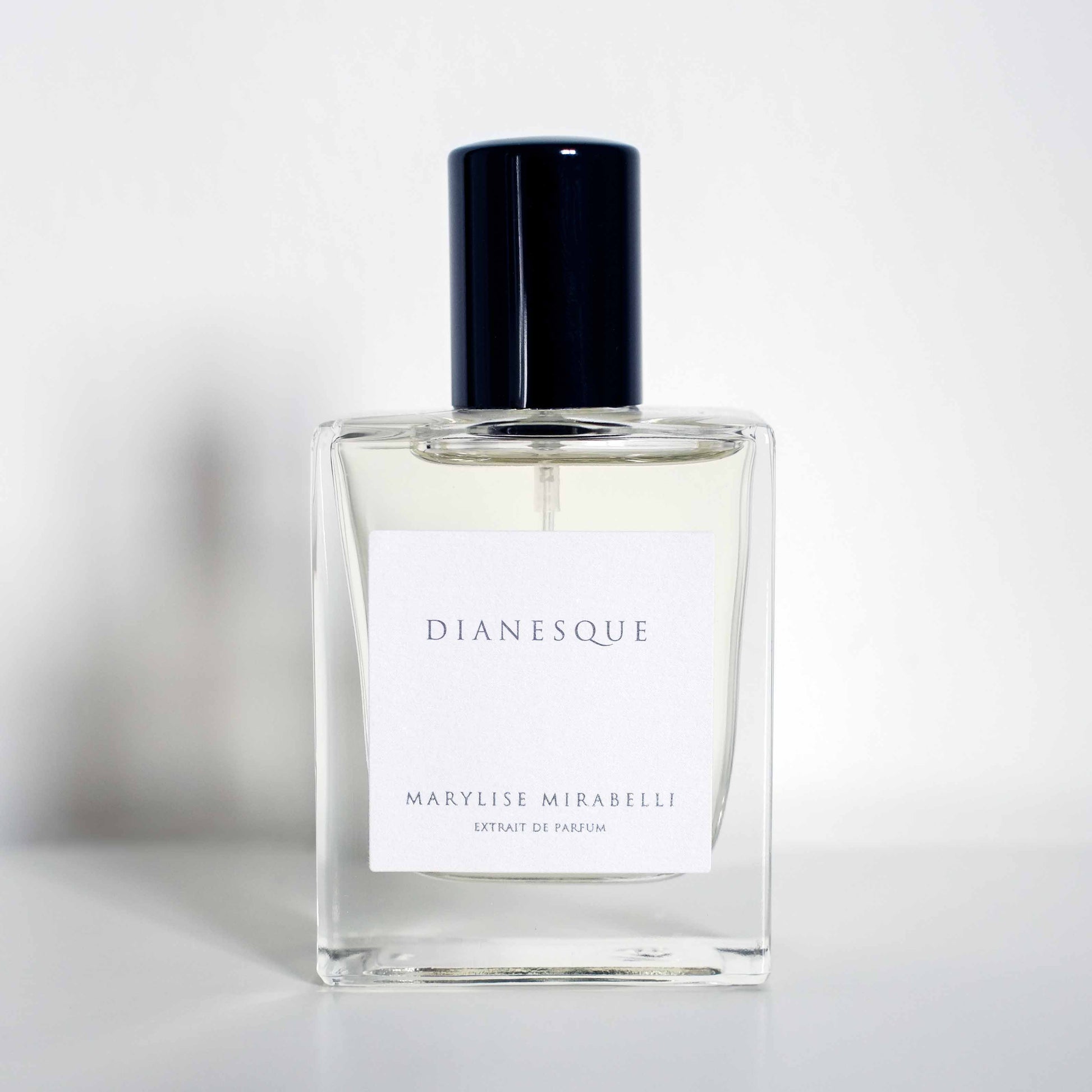 Flacon sobre et rectangulaire avec étiquette blanche et bouchon noir brillant, posé sur un fond blanc. Sur l'étiquette il est inscrit Dianesque en haut et Marylise Mirabelli Extrait de parfum en bas.