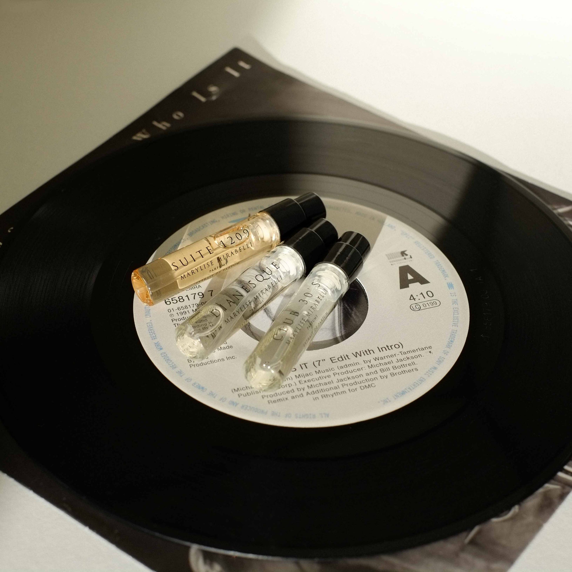 Le Set Découverte composé de 3 mini flacons en format 2ml disposé sur un disque vinyl 45 tours "Who is it" de Michael Jackson. La photo est baignée de la lumière du soleil.