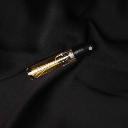 Un flacon de parfum avec son jus ambré en format 2ml du parfum Suite 1209 est posé sur un tissu en satin noir.